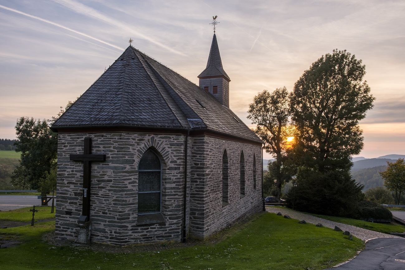 Eine steinerne Kapelle umgeben von grüner Wiese mit der untergehenden Sonne im Hintergrund. Eine steinerne Kapelle umgeben von grüner Wiese mit der untergehenden Sonne im Hintergrund.